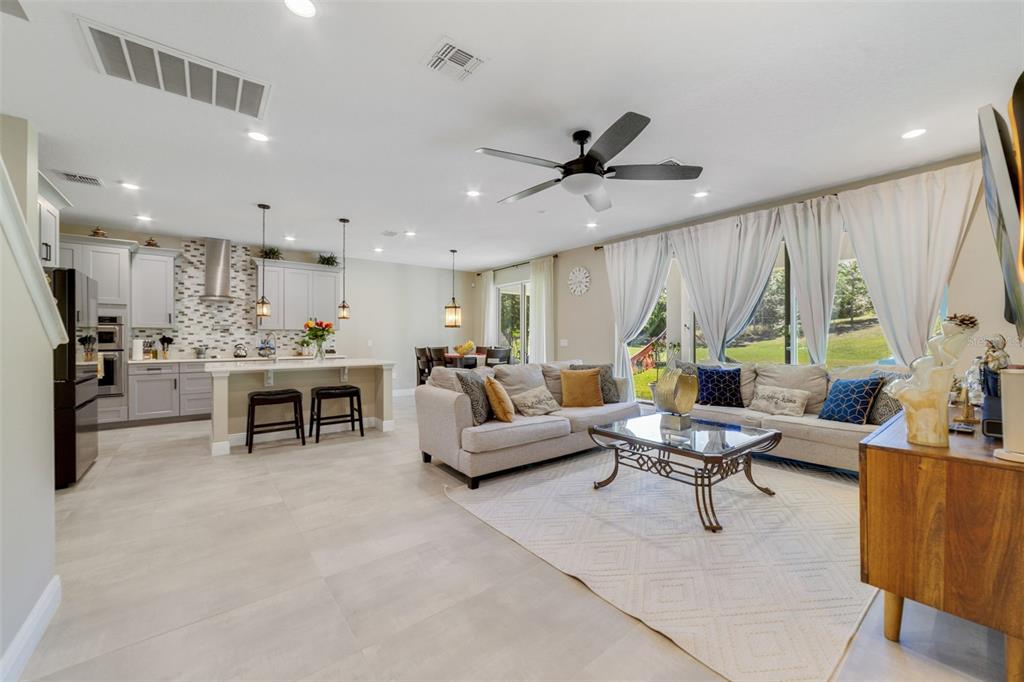 An open-concept living room and kitchen featuring light tile floors, neutral furniture, and large windows — 1970 STANDING ROCK CIRCLE, OAKLAND, FL