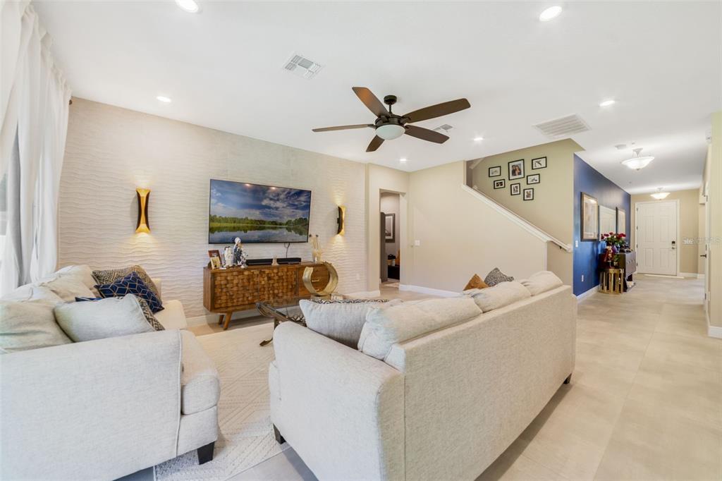 A living room features a textured accent wall, a television, two sofas, and a staircase — 1970 STANDING ROCK CIRCLE, OAKLAND, FL