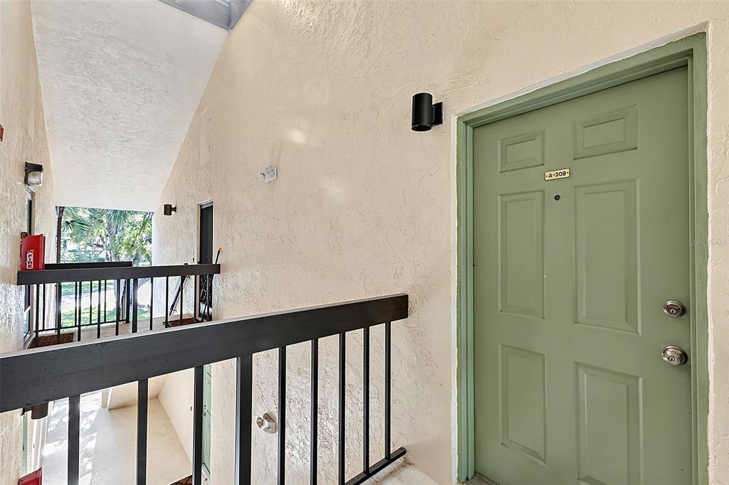 An exterior view of an apartment building hallway featuring a green door labeled A-208 — 19505 QUESADA AVENUE UNIT A208, PORT CHARLOTTE, FL