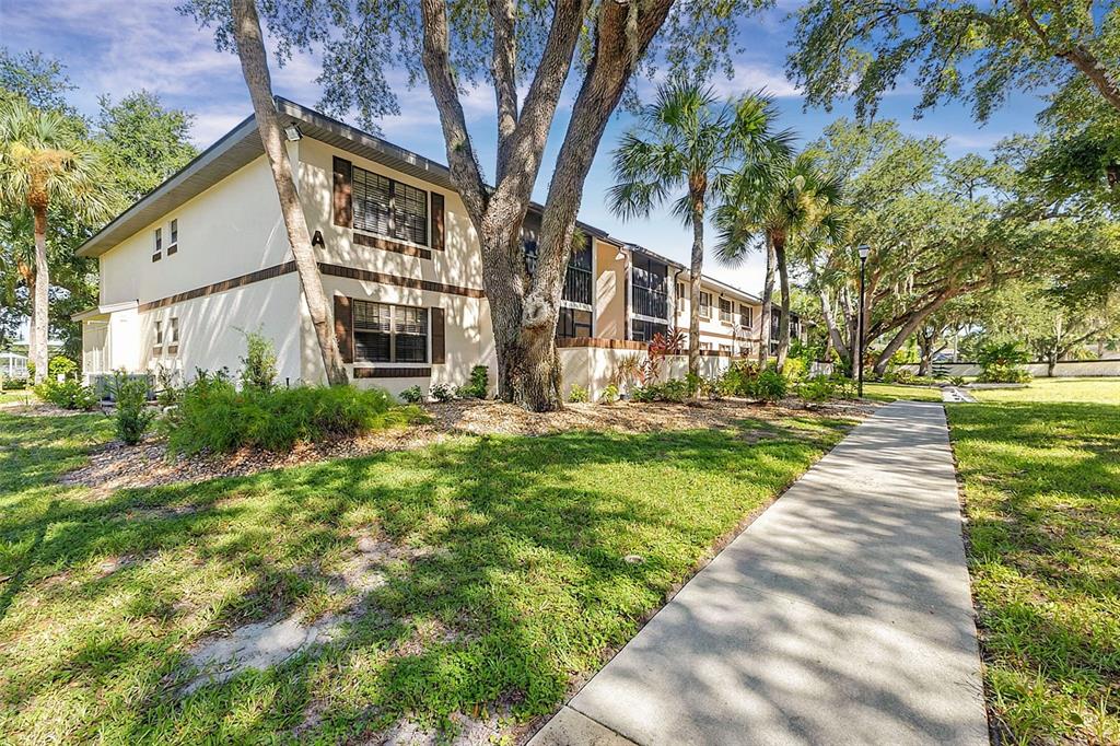 A two-story apartment building exterior features light-colored walls, brown shutters, and mature trees — 19505 QUESADA AVENUE UNIT A208, PORT CHARLOTTE, FL