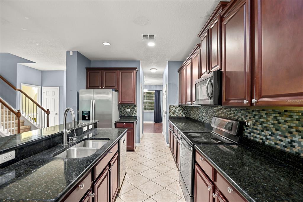 A kitchen features dark wood cabinets, black granite countertops, a tile floor, and stainless appliances — 925 COUNTS CREST CIRCLE, APOPKA, FL