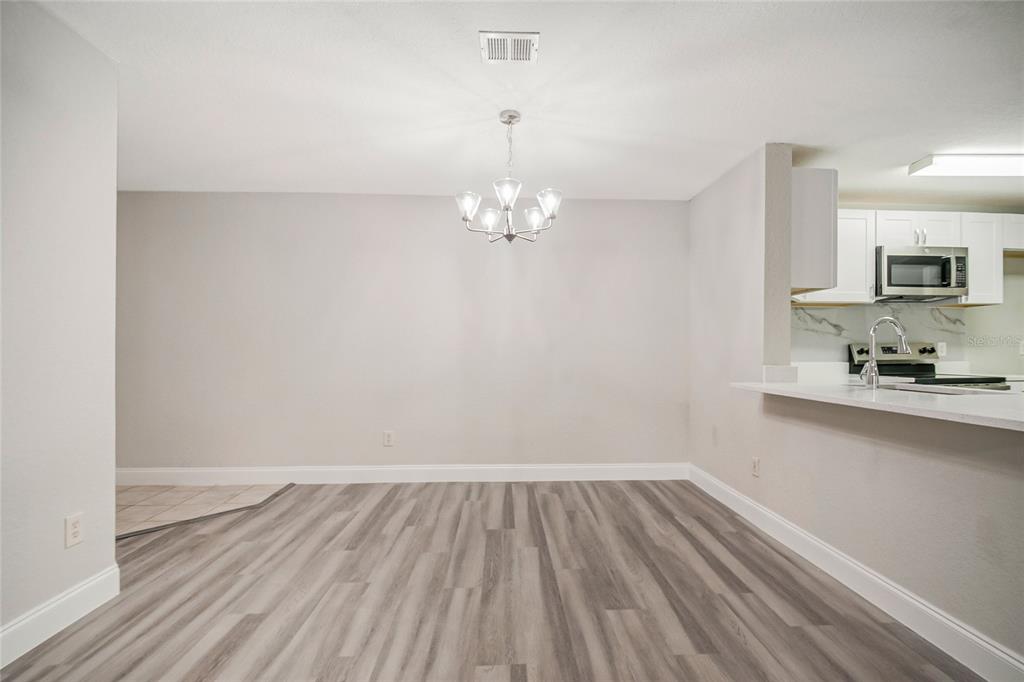 An open living area features light wood-look flooring, a chandelier, and a white front door — 7511 SEURAT STREET UNIT 10102, ORLANDO, FL