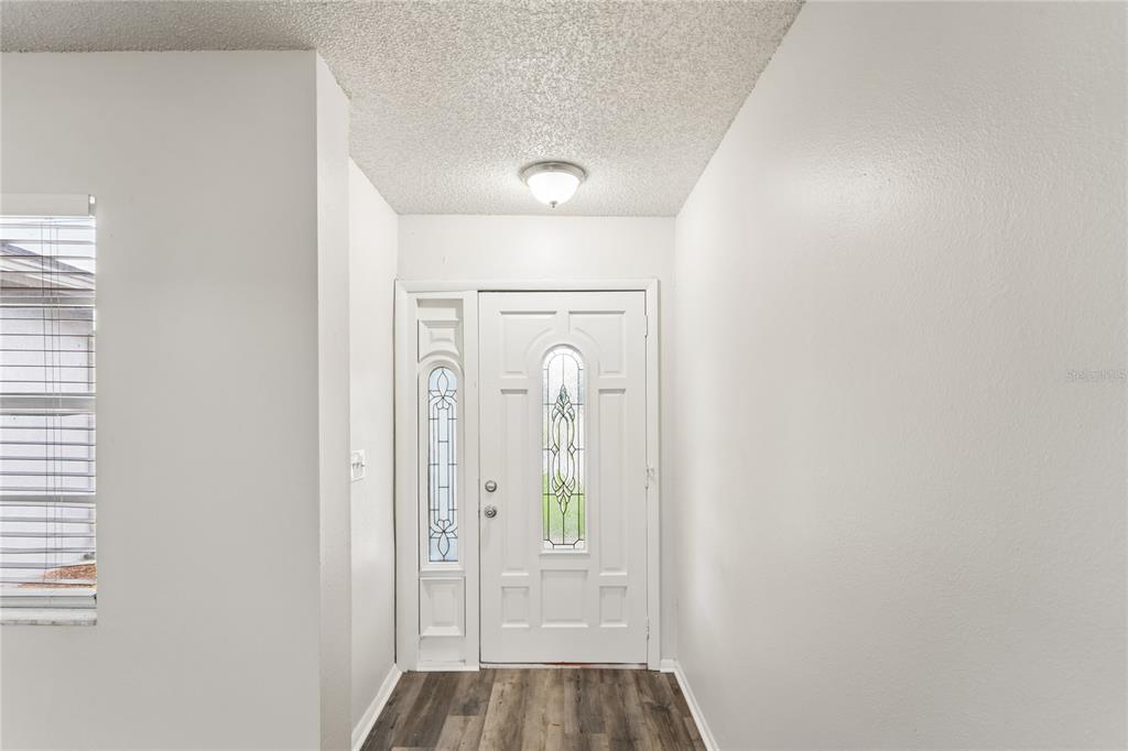 An entryway features a white front door with decorative glass, a ceiling light, and wood-look flooring — 10275 56TH STREET N, PINELLAS PARK, FL