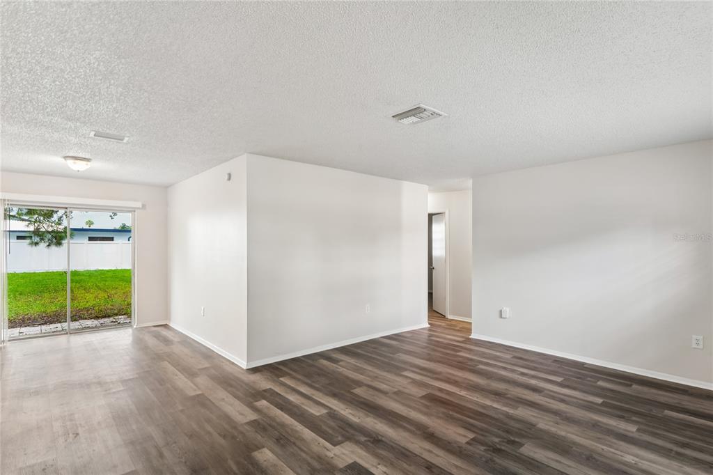 An empty living room with wood-look flooring, white walls, and a sliding glass door — 10275 56TH STREET N, PINELLAS PARK, FL