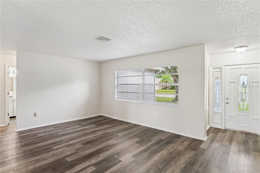 An empty living room with light gray walls, wood-look flooring, and a white front door — 10275 56TH STREET N, PINELLAS PARK, FL