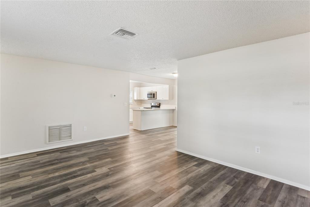 An open-concept living area features wood-look flooring and a view into a white kitchen — 10275 56TH STREET N, PINELLAS PARK, FL