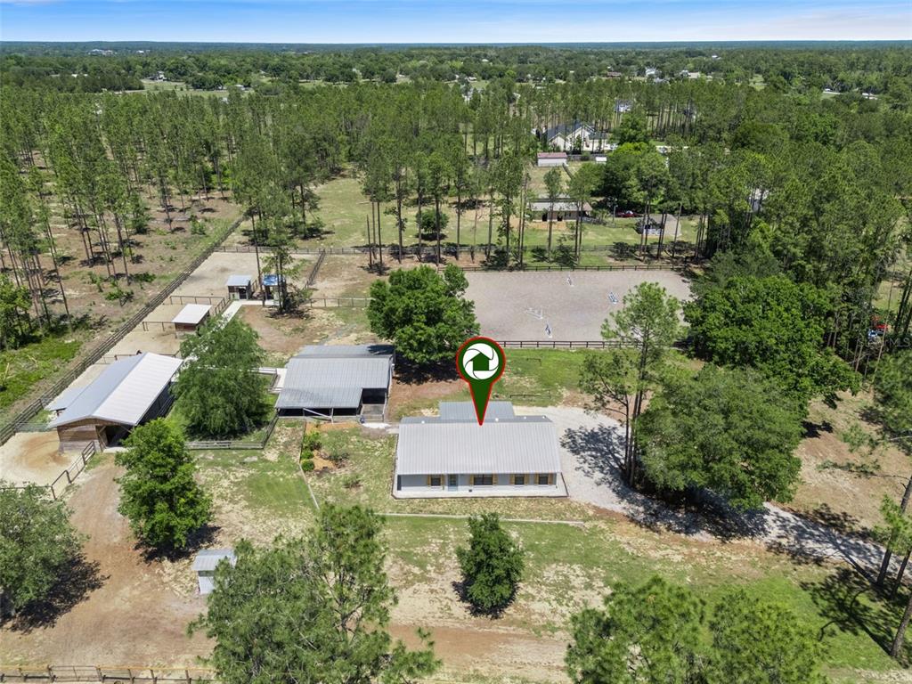 An aerial view shows a house with a metal roof, outbuildings, and a riding arena — 20701 COUNTY ROAD 44A, EUSTIS, FL
