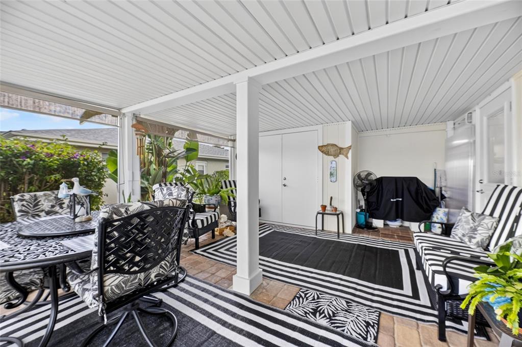 A covered patio features a dining set, striped outdoor rugs, and a seating area — 1516 NEW BEDFORD DRIVE, SUN CITY CENTER, FL