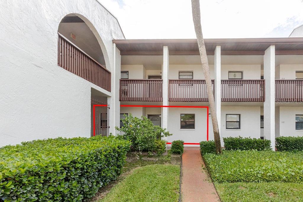 A ground-level apartment exterior features a white stucco wall, a window, and a gated entrance — 7623 RADCLIFFE CIRCLE UNIT 111A, PORT RICHEY, FL