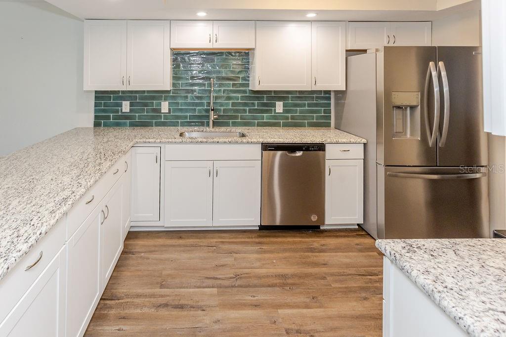 A kitchen with white cabinets, granite countertops, a green tile backsplash, and stainless steel appliances — 7623 RADCLIFFE CIRCLE UNIT 111A, PORT RICHEY, FL