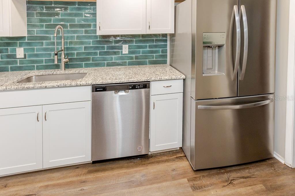 A kitchen features white cabinets, a teal subway tile backsplash, granite countertops, and stainless appliances — 7623 RADCLIFFE CIRCLE UNIT 111A, PORT RICHEY, FL