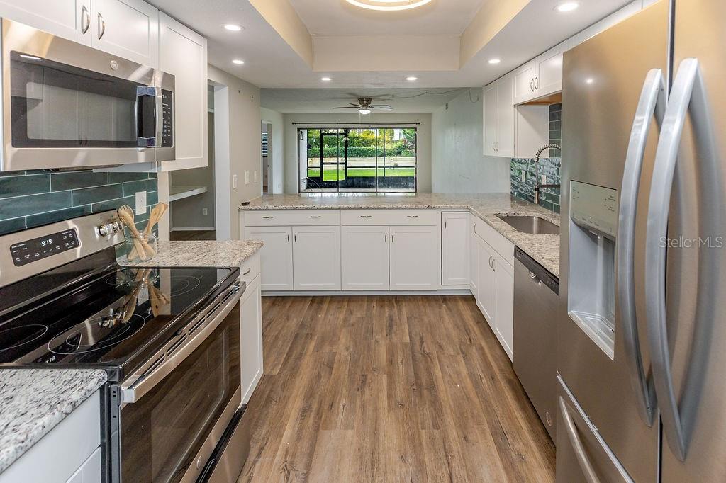 A kitchen with white cabinets, granite countertops, stainless steel appliances, and wood-look flooring — 7623 RADCLIFFE CIRCLE UNIT 111A, PORT RICHEY, FL