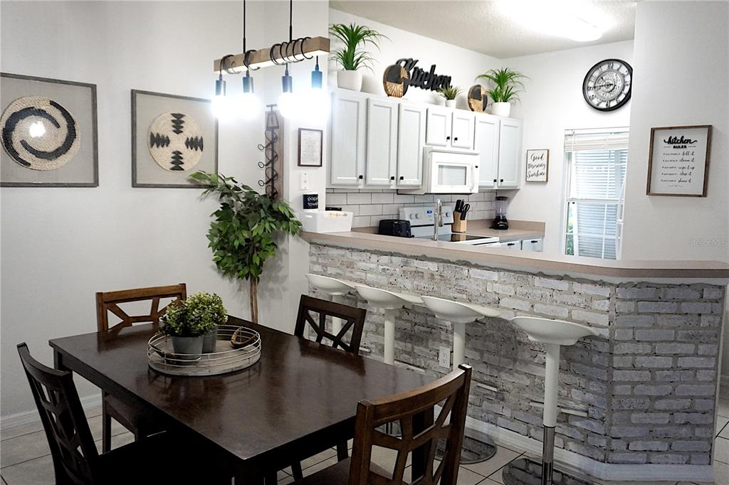 A dining area with a dark wood table sits adjacent to a kitchen with bar seating — 8529 BAY LILLY LOOP, KISSIMMEE, FL