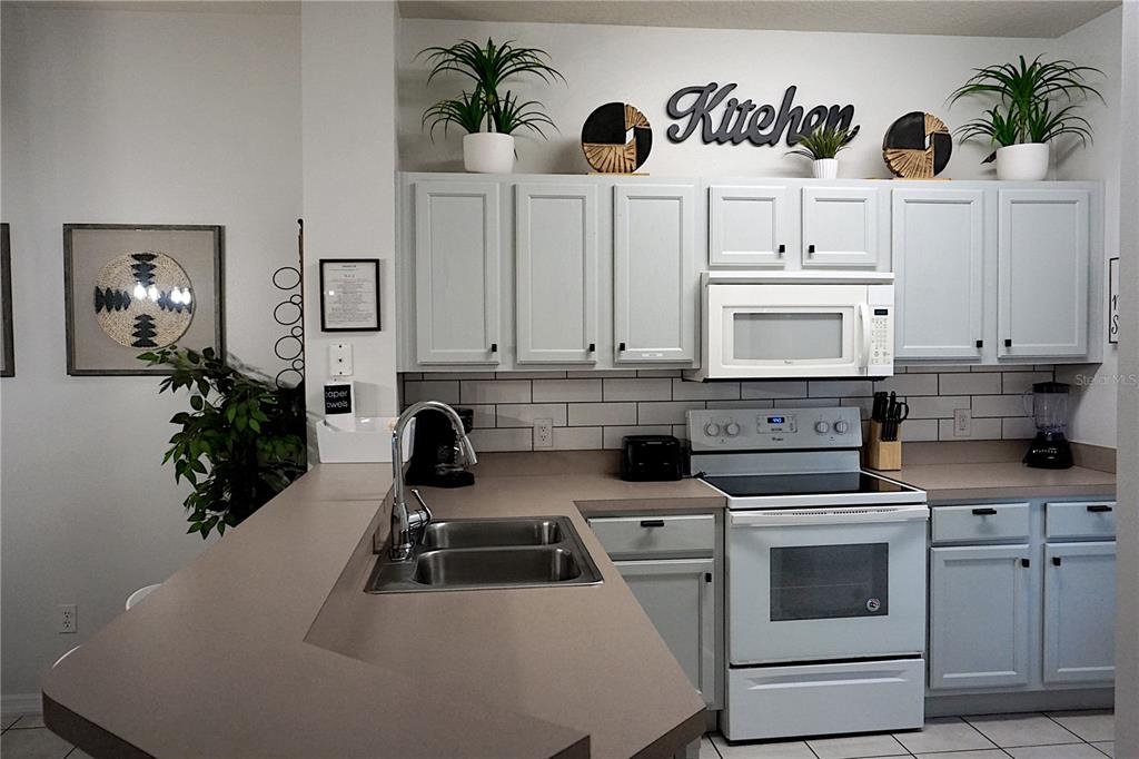 A kitchen features light gray cabinets, white appliances, a double sink, and a tiled backsplash — 8529 BAY LILLY LOOP, KISSIMMEE, FL