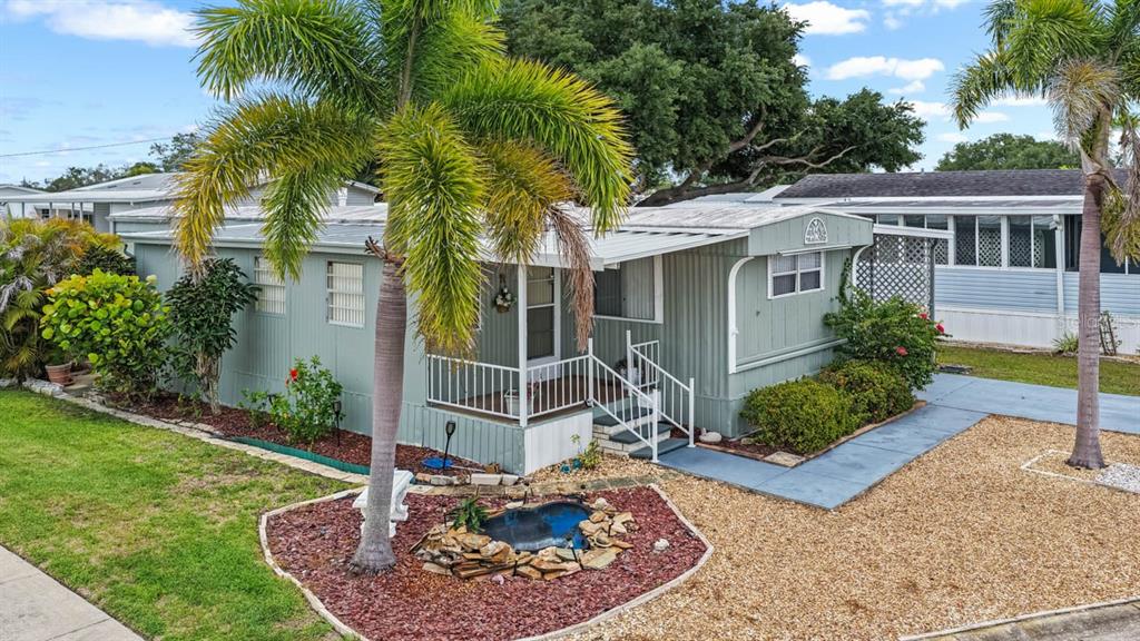 A light green mobile home features a front porch, palm trees, and a small rock pond — 123 SAINT KITTS WAY, APOLLO BEACH, FL