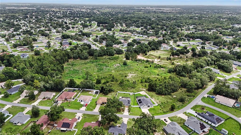 An aerial view shows a residential neighborhood surrounding a large, undeveloped grassy lot — 11303 SW 62ND CIRCLE, OCALA, FL