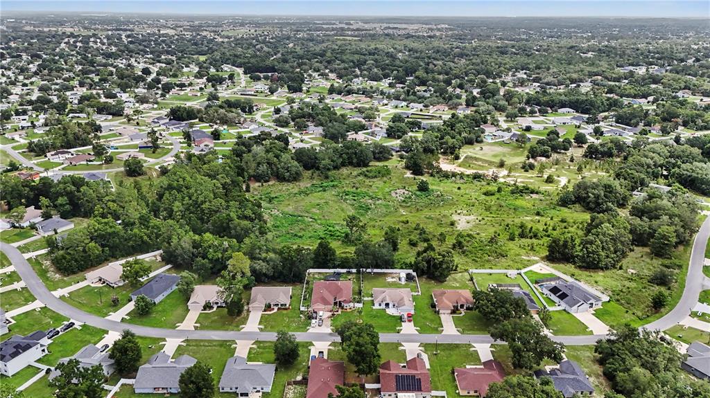 An aerial view shows a suburban neighborhood with houses bordering a large, undeveloped grassy lot — 11303 SW 62ND CIRCLE, OCALA, FL