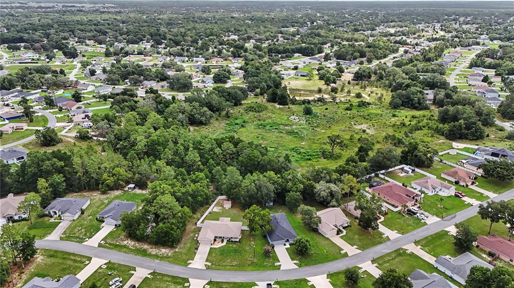 An aerial view shows a suburban neighborhood with houses bordering a large, undeveloped wooded lot — 11303 SW 62ND CIRCLE, OCALA, FL
