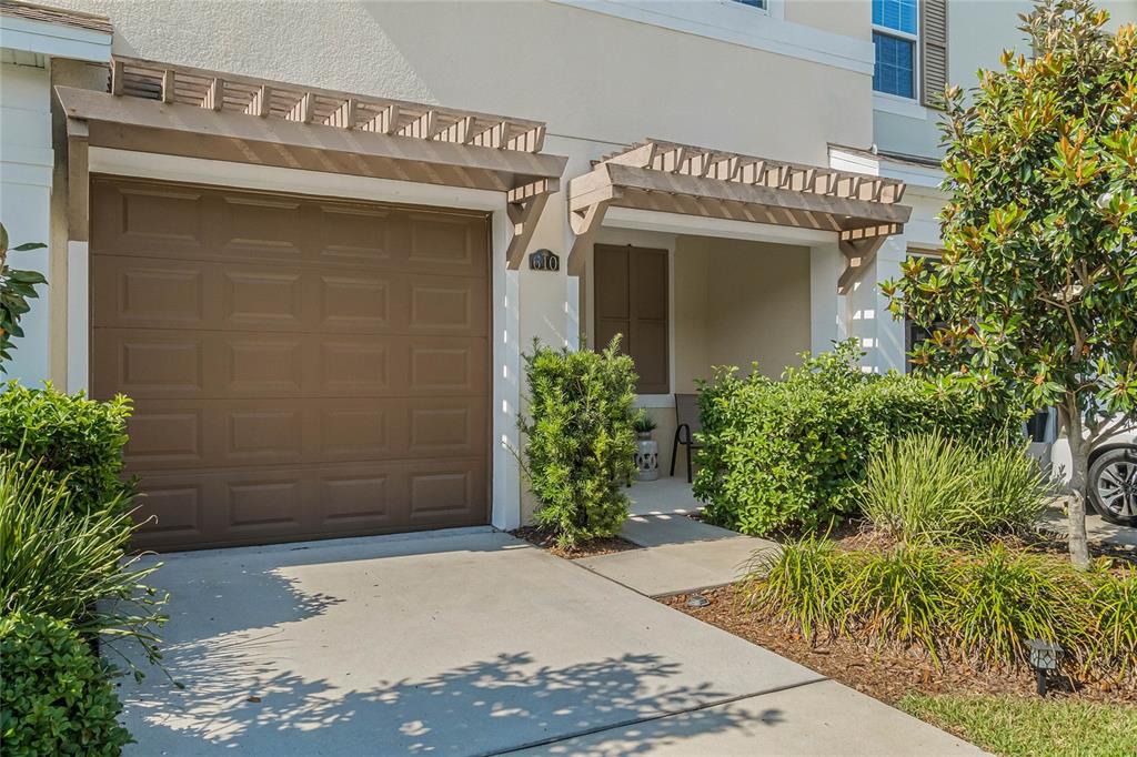 The exterior of a townhouse features a brown garage door, a covered entryway, and landscaping — 610 FORTANINI CIRCLE, OCOEE, FL