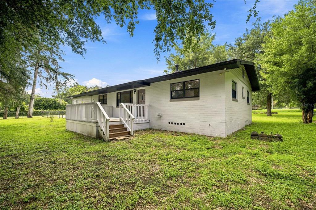 A white brick house with a wooden deck and black trim sits on a grassy lot — 455 SW 73RD STREET ROAD, OCALA, FL