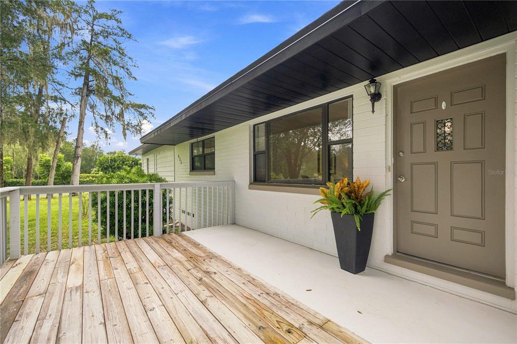 A wooden deck leads to the front entrance of a white brick house with a door — 455 SW 73RD STREET ROAD, OCALA, FL
