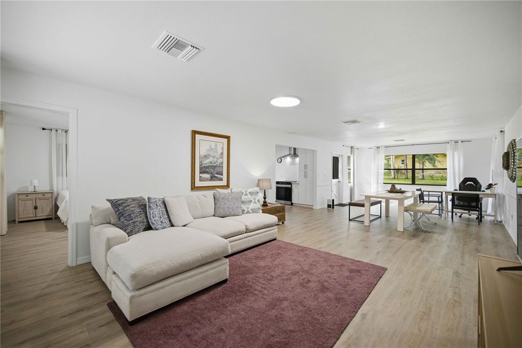 A spacious open-concept living and dining area features light wood flooring and a sectional sofa — 455 SW 73RD STREET ROAD, OCALA, FL