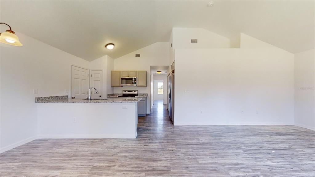 A kitchen with granite countertops and light wood cabinets overlooks a spacious living area — 13725 SW 111TH LANE, DUNNELLON, FL