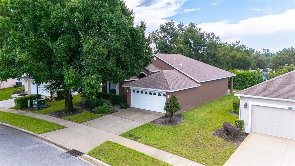 An aerial view of a brown suburban house with a white garage and large tree — 8034 ARCADIAN COURT, MOUNT DORA, FL