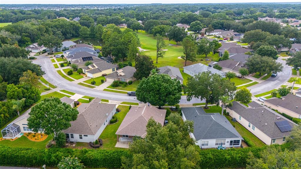 An aerial view shows a suburban neighborhood with houses, green lawns, and a golf course — 8034 ARCADIAN COURT, MOUNT DORA, FL