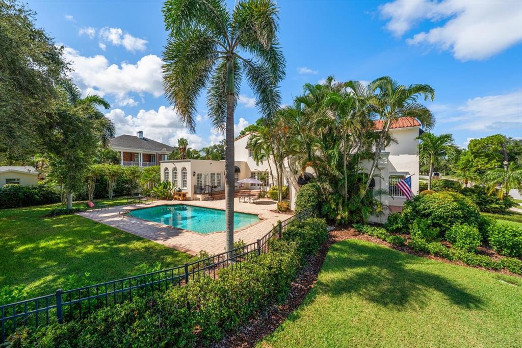 A backyard featuring a swimming pool, patio, palm trees, and a two-story stucco house — 561 PALMETTO ROAD, BELLEAIR, FL