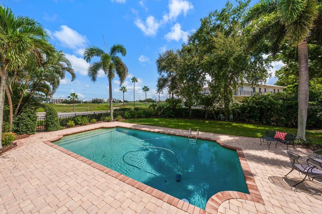 A backyard swimming pool with a brick paver deck, palm trees, and a grassy lawn — 561 PALMETTO ROAD, BELLEAIR, FL