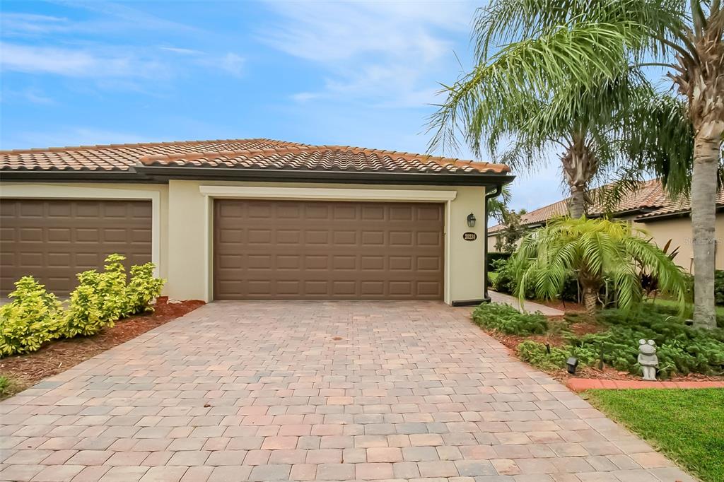 A paved driveway leads to a house with a brown garage door and palm trees — 20230 TESORO DRIVE, VENICE, FL