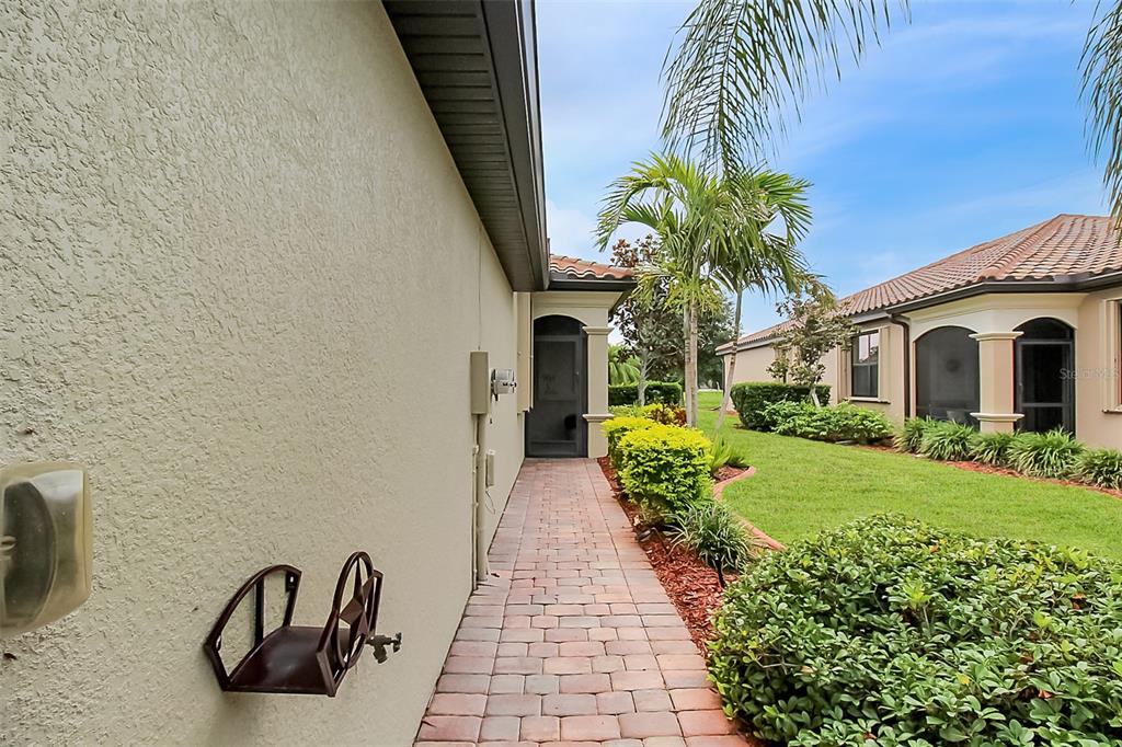 A paved walkway leads along the side of a house toward a screened entry door — 20230 TESORO DRIVE, VENICE, FL