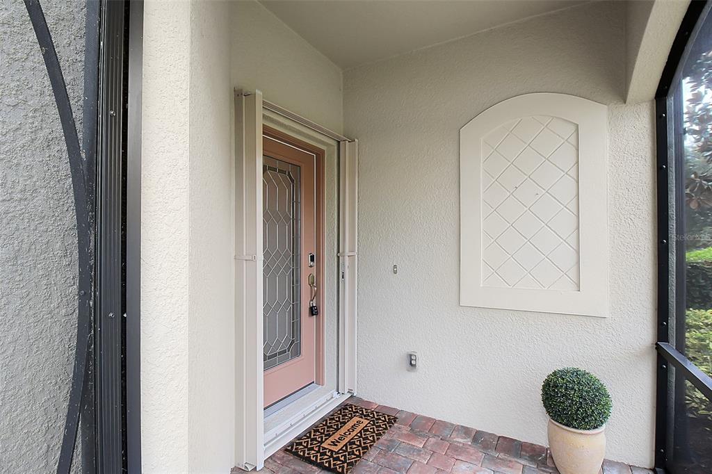 A covered entryway features a pink front door with a decorative glass insert and pavers — 20230 TESORO DRIVE, VENICE, FL
