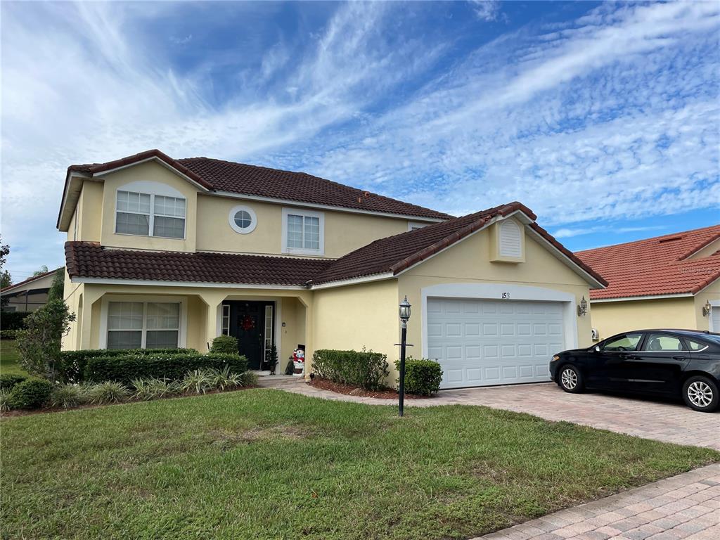 A two-story yellow house with a brown tile roof and a two-car garage — 153 HUMMINGBIRD PASS, DAVENPORT, FL