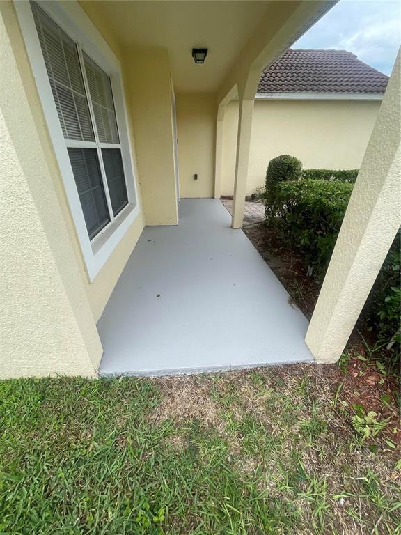 A covered concrete porch with a light gray painted floor sits beside a yellow house — 153 HUMMINGBIRD PASS, DAVENPORT, FL