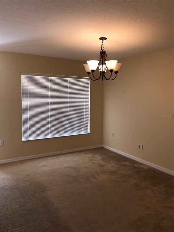 A carpeted dining room features a chandelier, a window with blinds, and beige walls — 153 HUMMINGBIRD PASS, DAVENPORT, FL