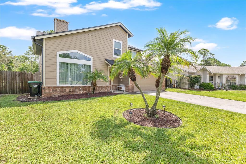 A two-story house with tan siding, a brick base, and a palm tree in the yard — 11296 CYPRESS LEAF DRIVE, ORLANDO, FL