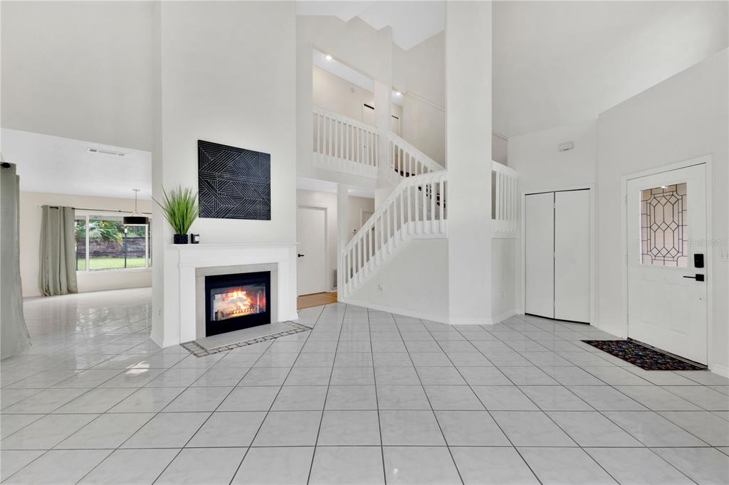 A bright foyer features white tile floors, a fireplace, and a staircase leading to a loft — 11296 CYPRESS LEAF DRIVE, ORLANDO, FL