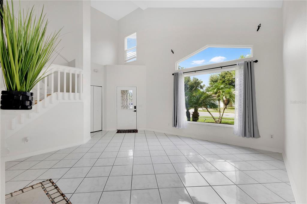 A bright, tiled entryway features a high vaulted ceiling, a staircase, and a large window — 11296 CYPRESS LEAF DRIVE, ORLANDO, FL