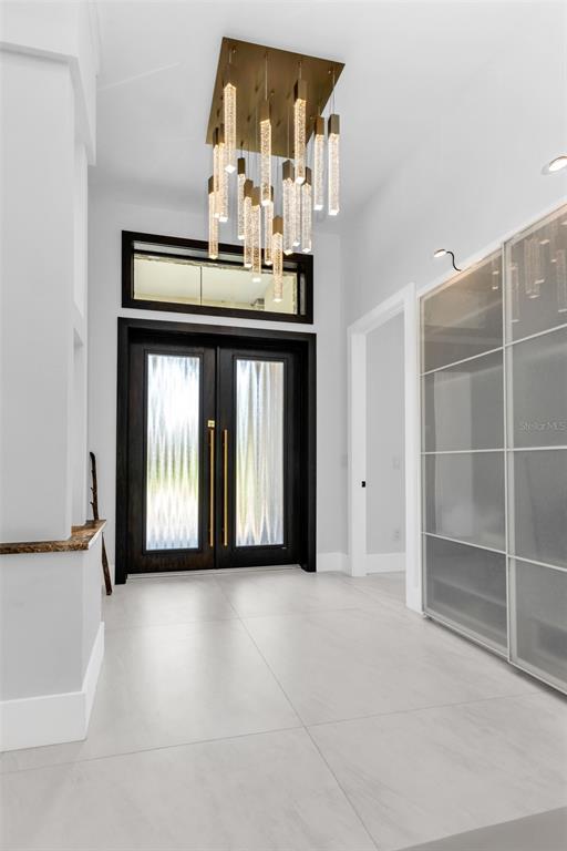 A modern entryway features a crystal chandelier, double front doors, and large light-colored floor tiles — 115 SOLANA STREET, NORTH PORT, FL