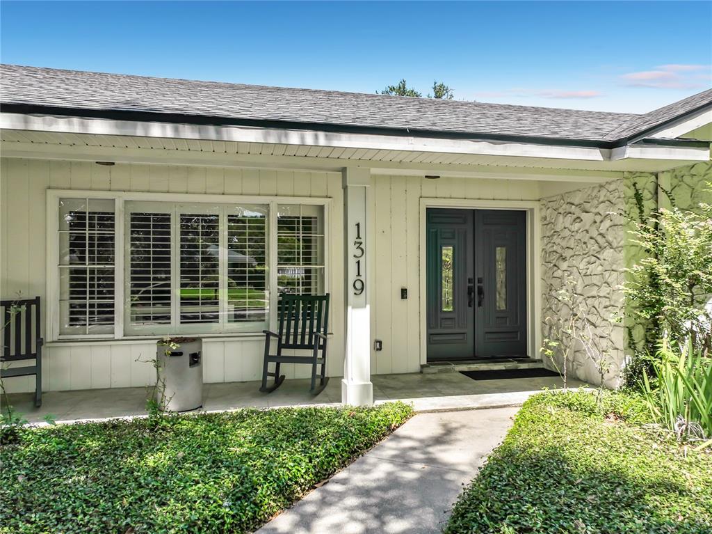 A front porch features a dark double door, a rocking chair, and stone wall accents — 1319 BUCKWOOD DRIVE, ORLANDO, FL
