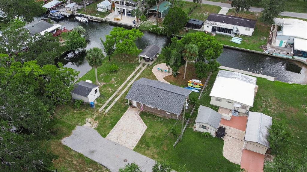 An aerial view shows a house with a gray roof, a shed, and a canal — 5411 TEAL DRIVE, WEEKI WACHEE, FL