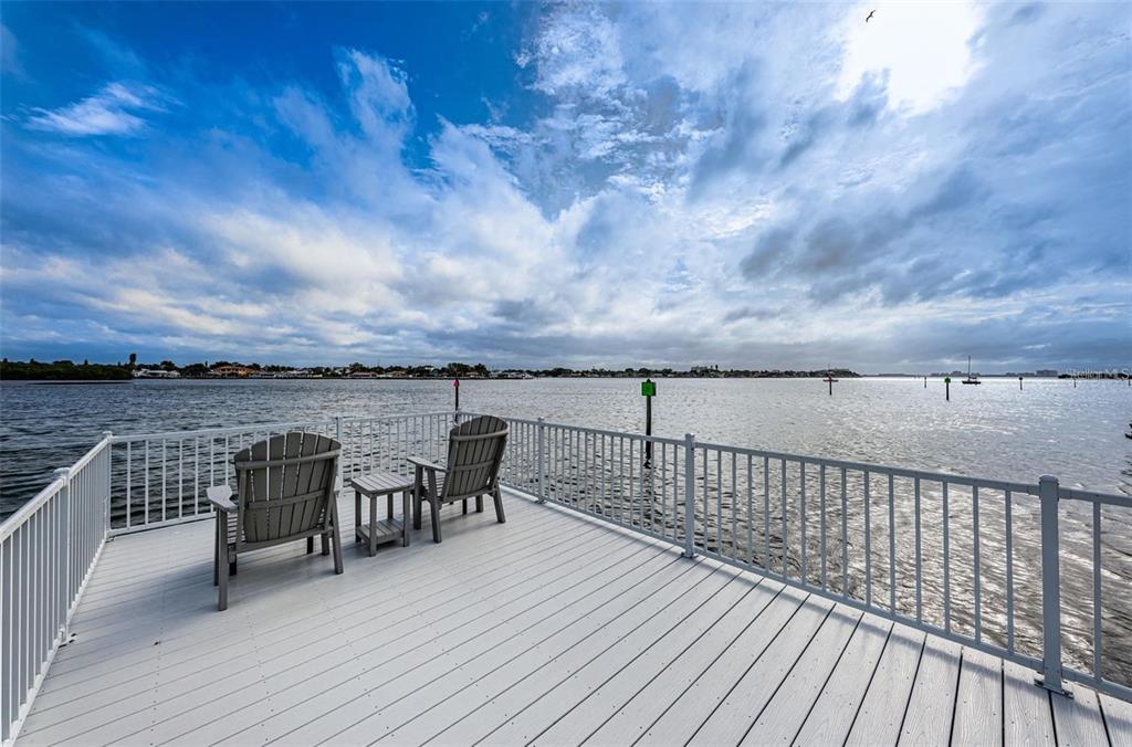 A spacious outdoor deck features multiple chairs and lounge chairs overlooking a body of water — 1859 SHORE DRIVE S UNIT 107, SOUTH PASADENA, FL