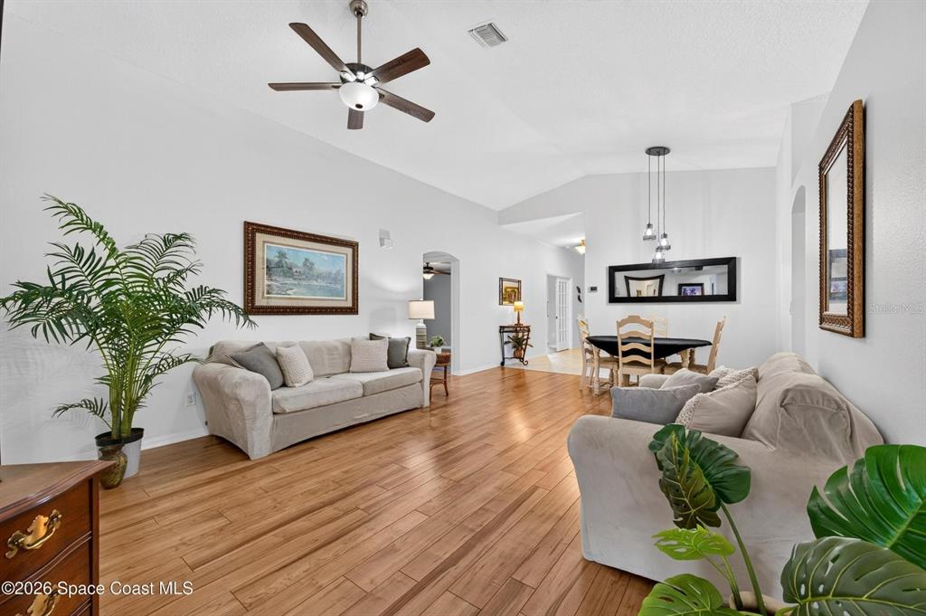 A living and dining area features light-colored sofas, wood flooring, and a vaulted ceiling — 2336 DEERCROFT DRIVE, MELBOURNE, FL
