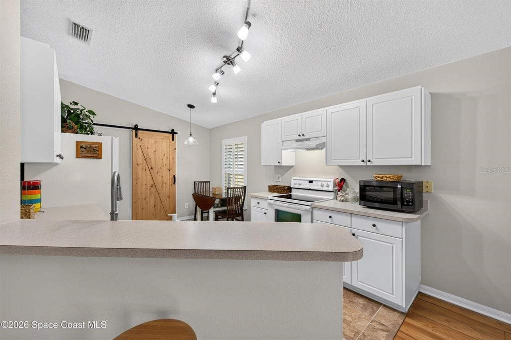 A kitchen features white cabinets, a breakfast bar, and a sliding barn door — 2336 DEERCROFT DRIVE, MELBOURNE, FL