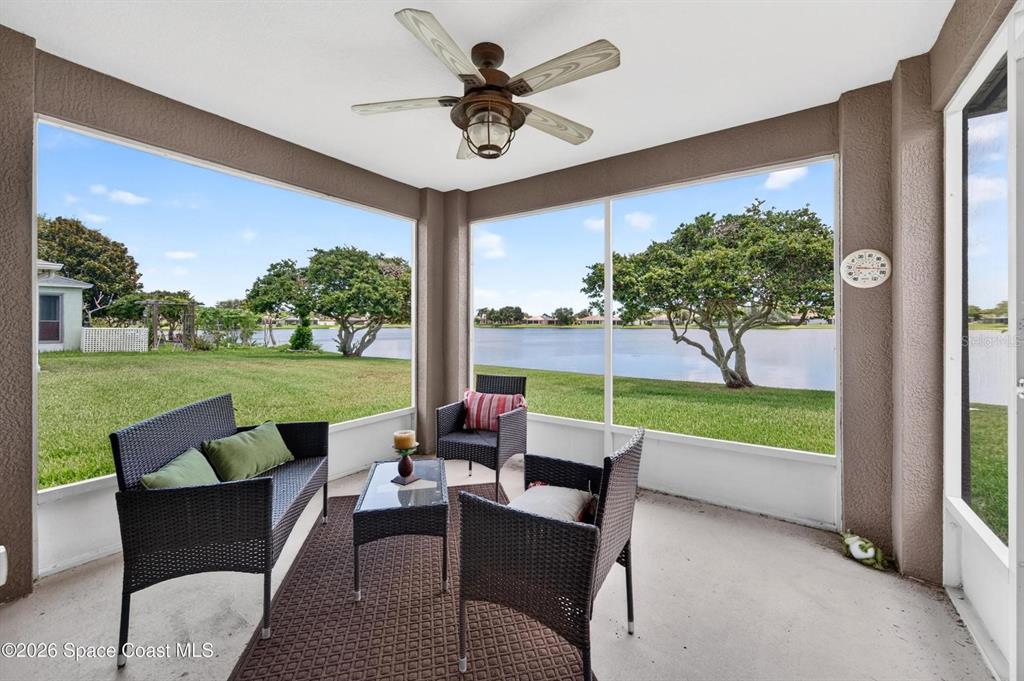 A screened-in patio features wicker furniture, a ceiling fan, and views of a lake — 2336 DEERCROFT DRIVE, MELBOURNE, FL