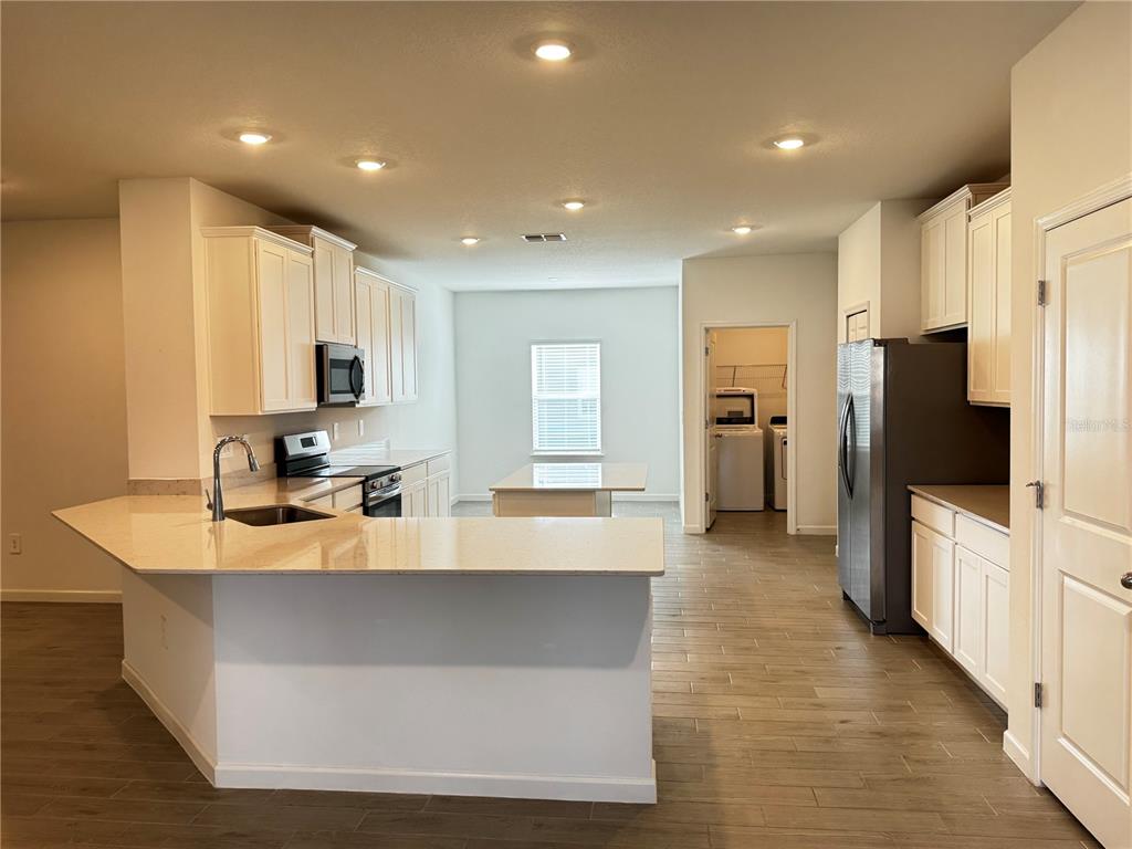 A kitchen features white cabinets, light countertops, stainless steel appliances, and wood-look tile flooring — 19447 SW 79TH STREET, DUNNELLON, FL