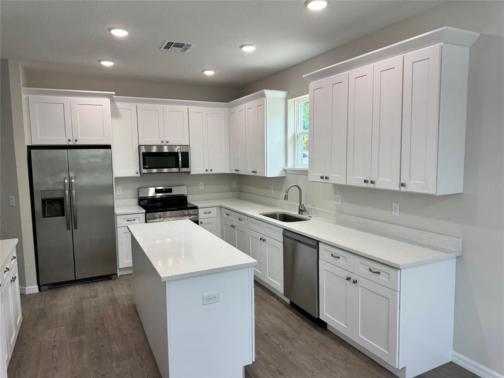 A modern kitchen features white cabinets, stainless steel appliances, a center island, and quartz countertops — 1013 FOOTE STREET, EUSTIS, FL