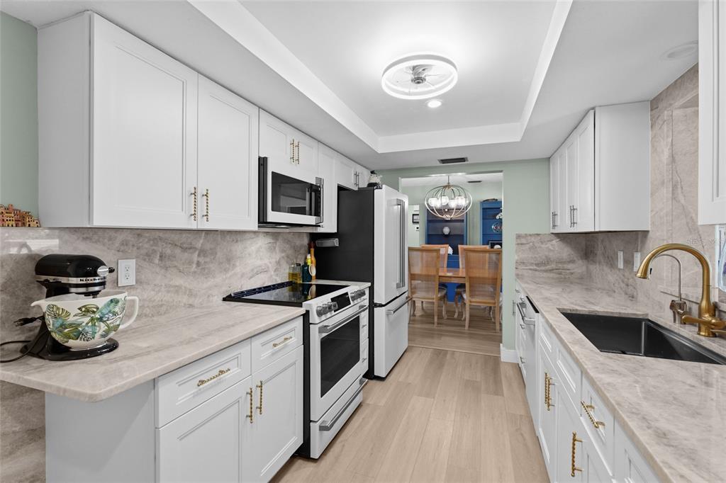 A modern kitchen features white cabinets, marble-look countertops, stainless steel appliances, and light wood flooring — 3274 SAVAGE ROAD, SARASOTA, FL